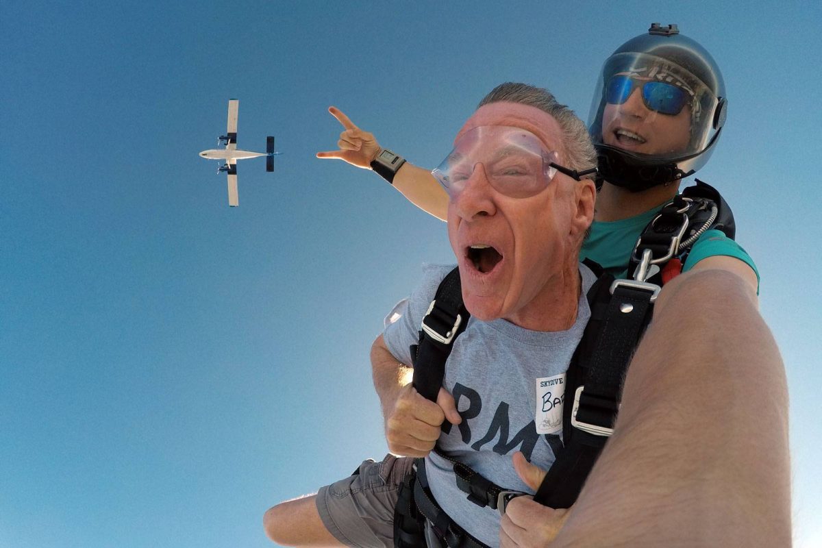 Male tandem skydiver enjoying freefall with Skydive City airplane above him.