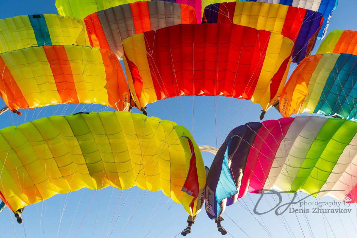 Skydivers with colorful canopies drifting toward the ground.