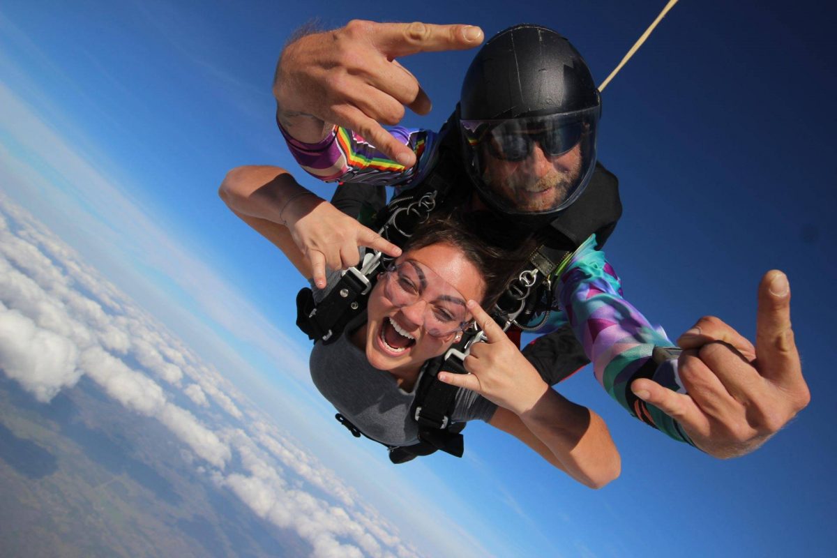 Female tandem skydiver and instructor giving rock on hand signs during free fall at Skydive City.
