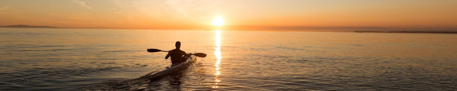 Man in kayak with sun setting in the distance.